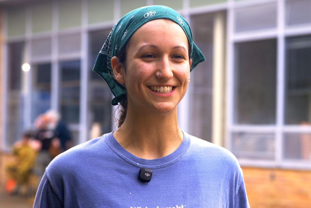 An instructor with a green bandana on her head smiling in an outdoor setting.