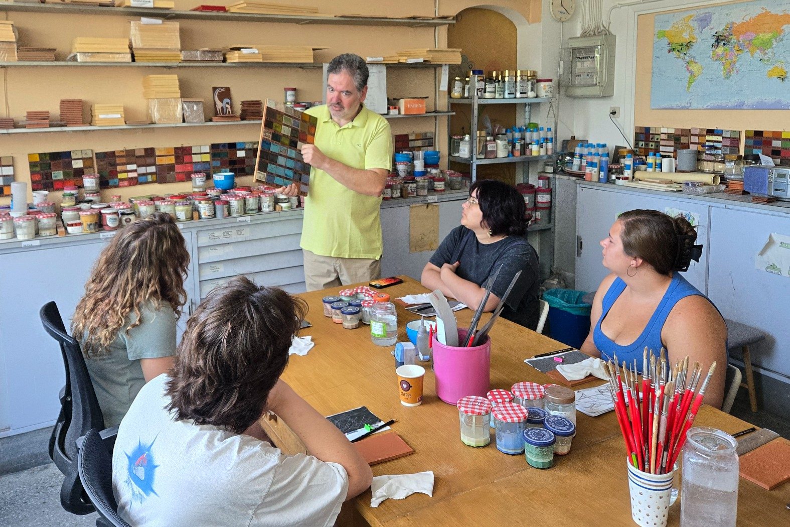 Instructor holds up a board of ceramic glaze samples while students gather around a table during the Ceramic Arts in Greece education abroad program.