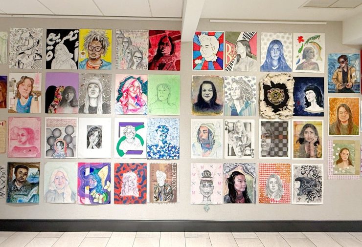 A large installation of student-created portraits in a variety of styles, colors, and media fills a wall as part of the 