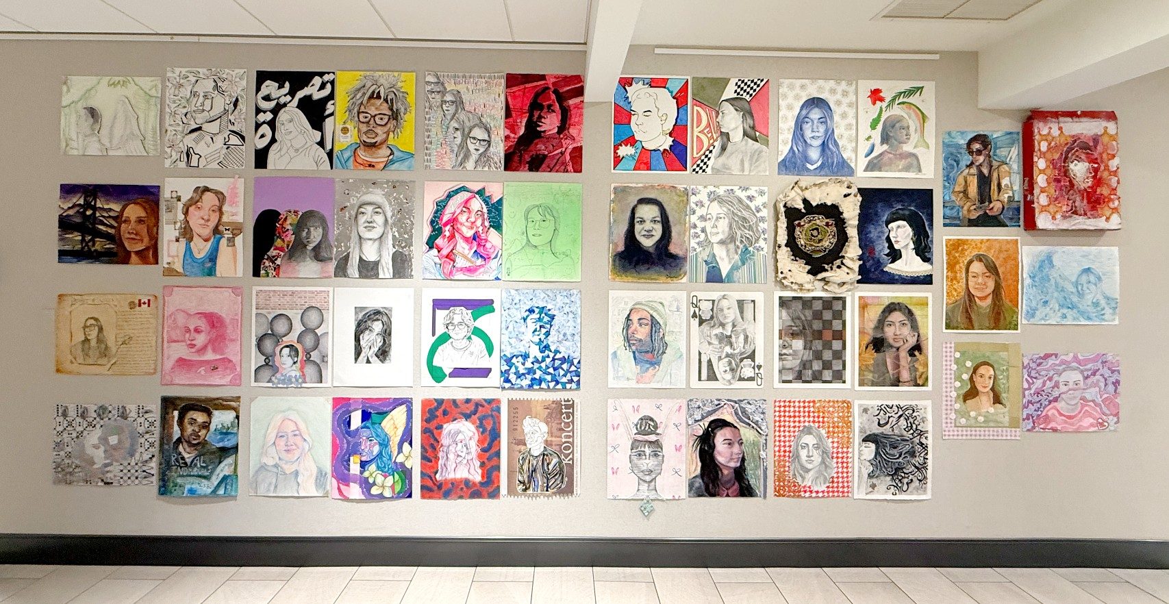 A large installation of student-created portraits in a variety of styles, colors, and media fills a wall as part of the 