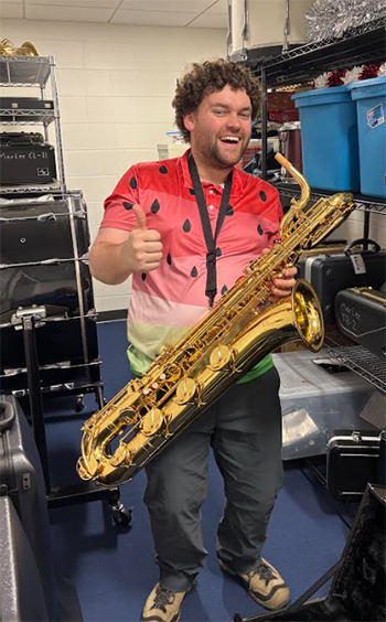 Educator Matthew Weber poses with a thumbs-up while holding a saxophone.
