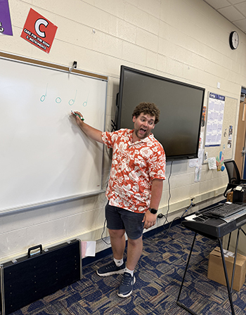 Mathew Weber stands in front of a white board drawing music notes.