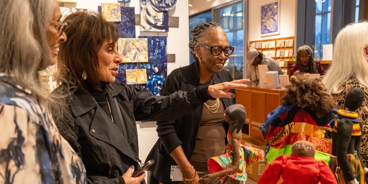 Gwendolyn Taylor smiles as she and several visitors gather around a display of handmade dolls dressed in colorful patterned fabrics.