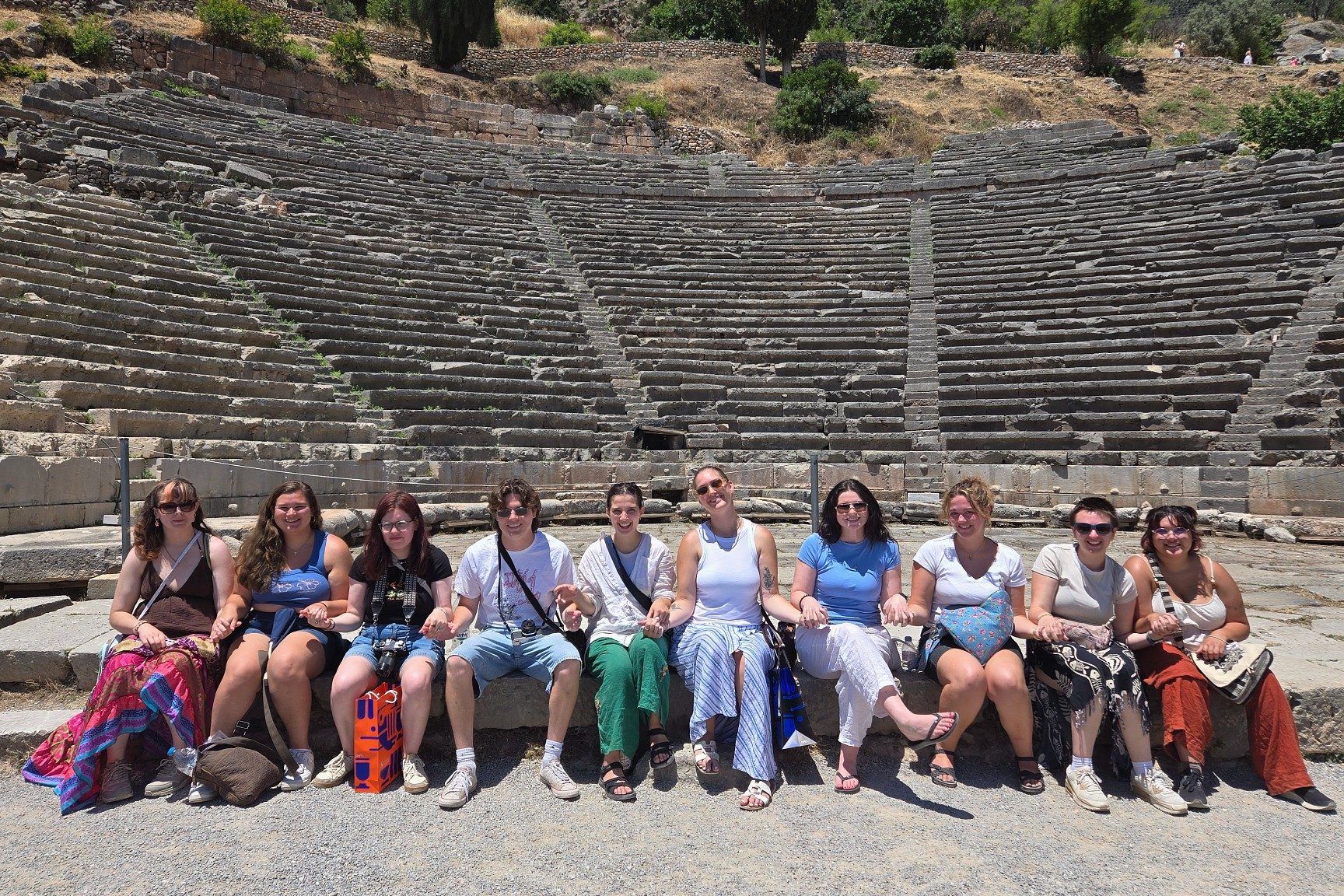 Students from the Ceramic Arts in Greece education abroad program sit together in front of the stone seating of an ancient Greek theater.