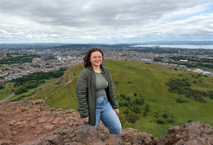 A person standing on a rocky overlook with a view of Edinburgh in the background.