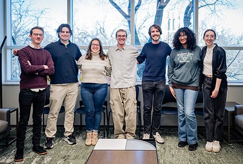 A group of seven student employees in front of a large window.